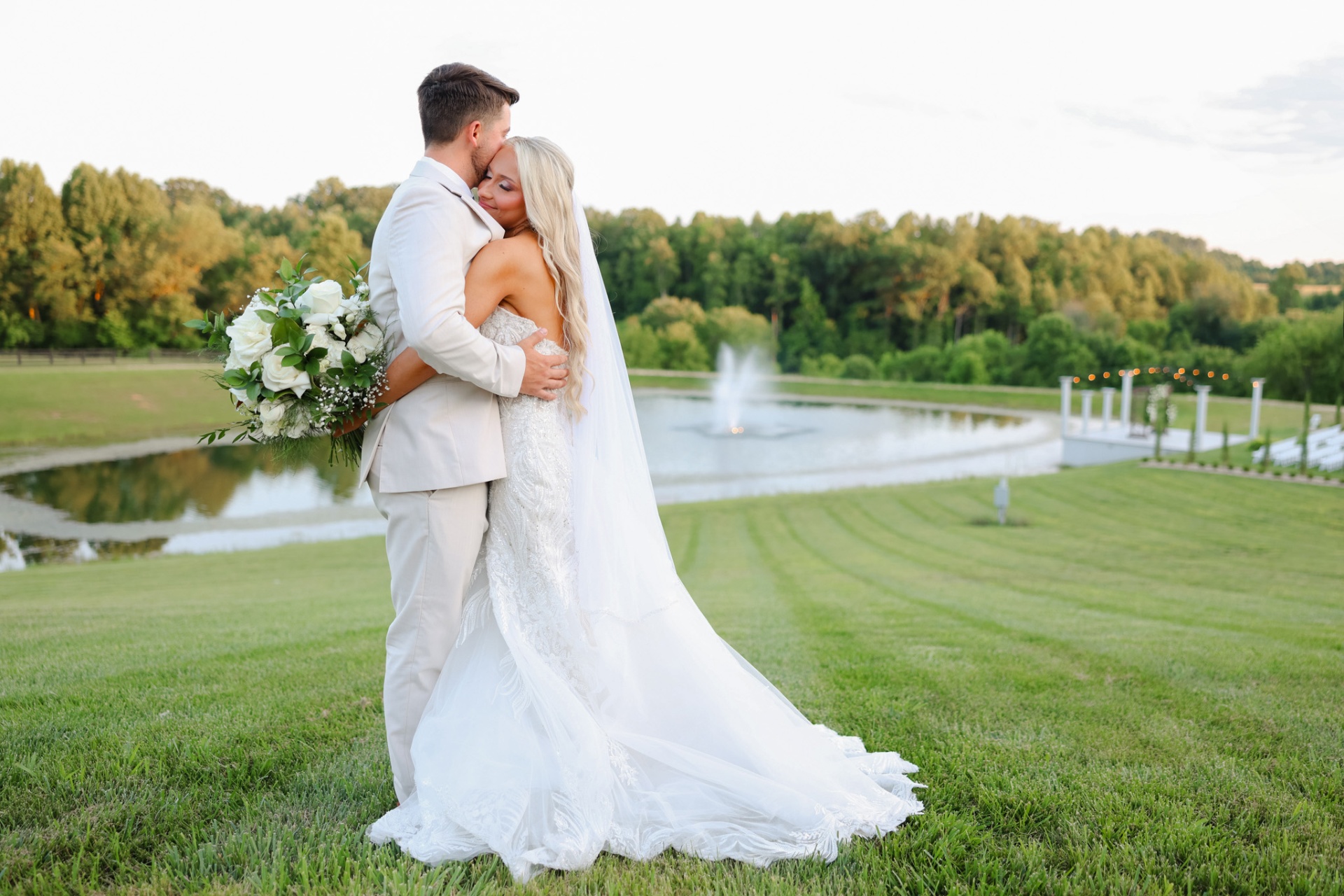 A bride and groom embracing by a lakeside fountain at golden hour