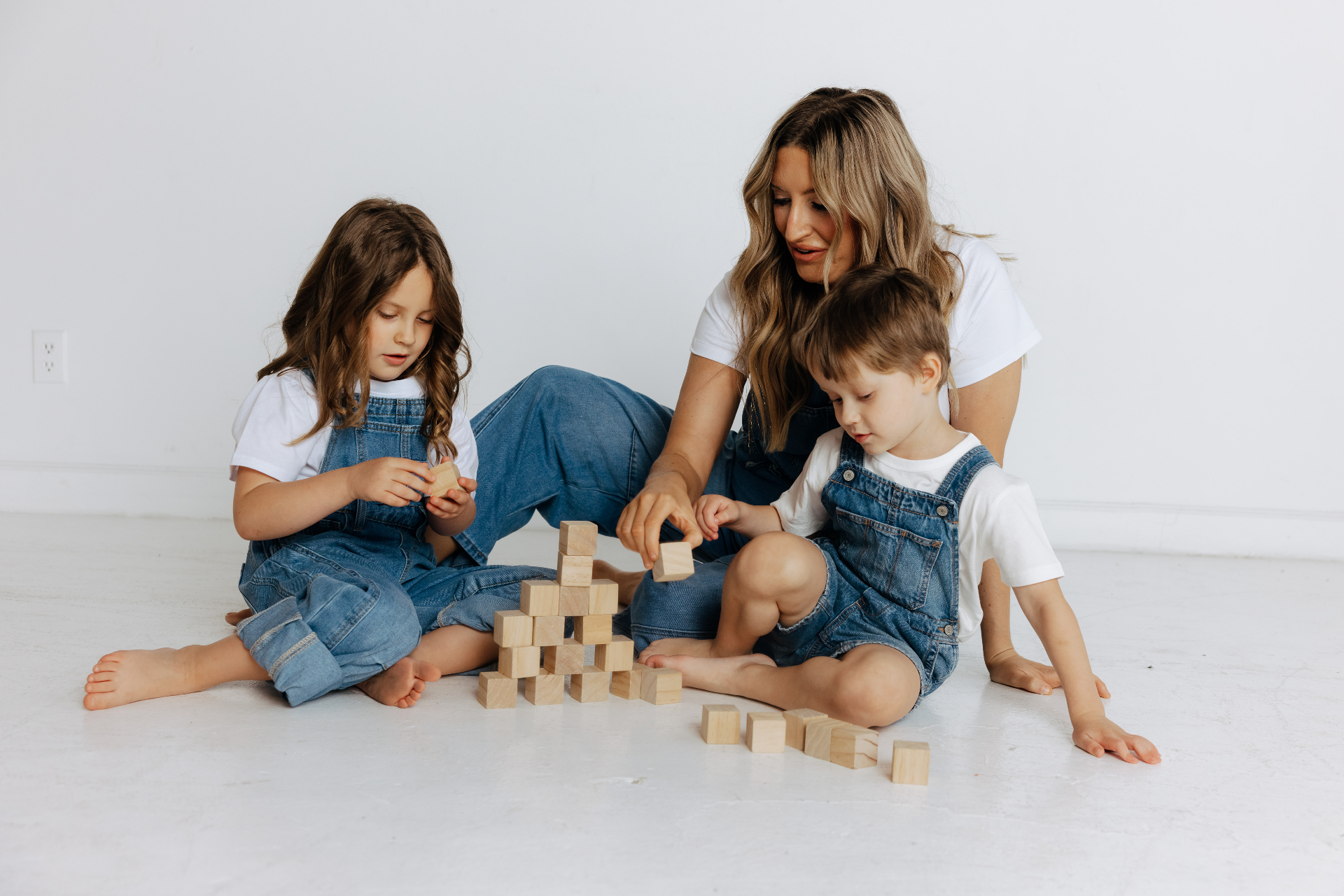 A mother and two young children playing with wooden blocks in a bright studio